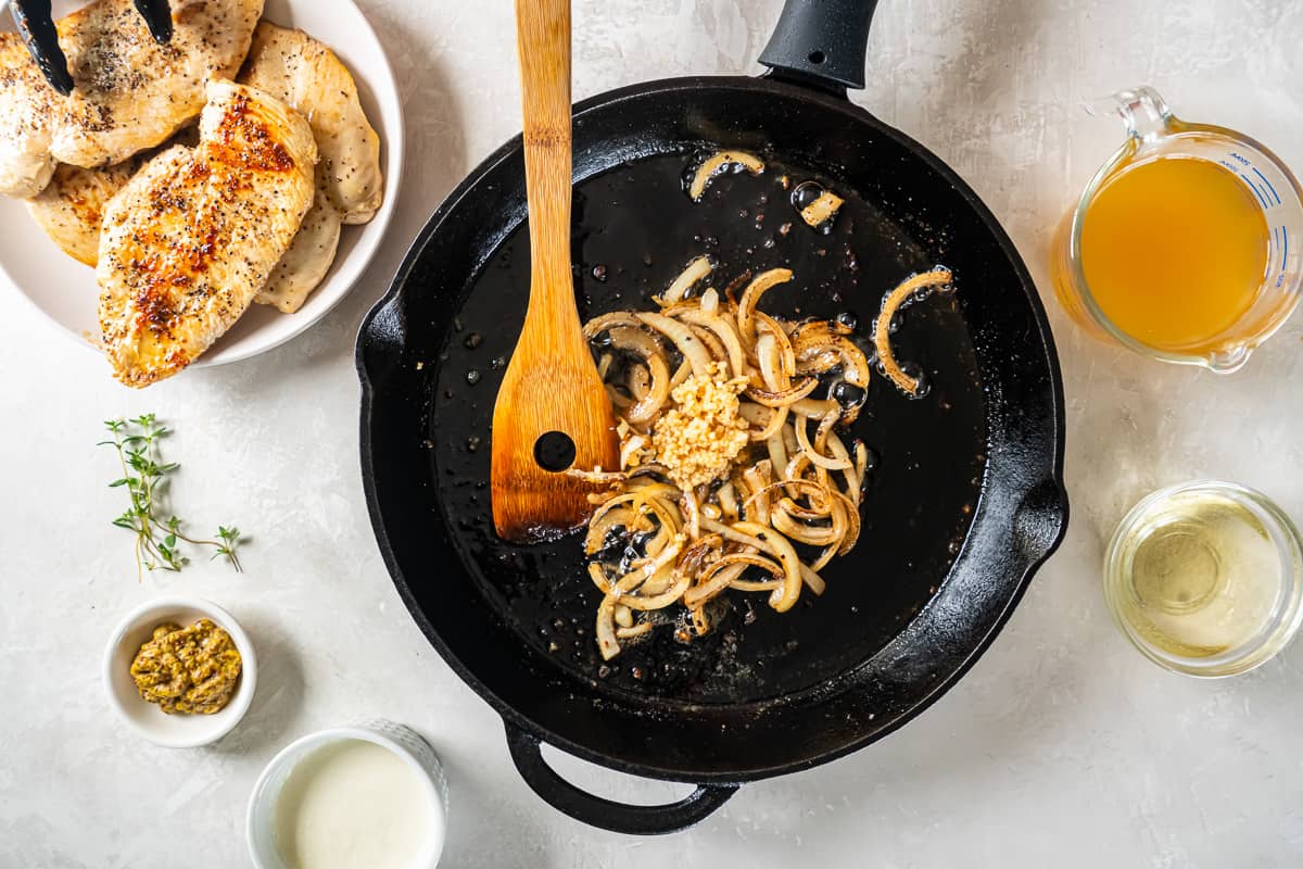 cooked sliced onion and garlic in a cast iron pan with a wooden spoon.