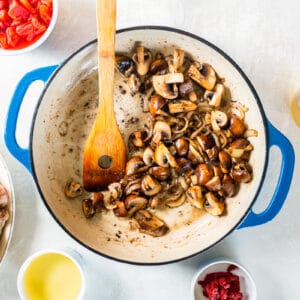 cooked onions and mushrooms in a blue pan with a wooden spoon.