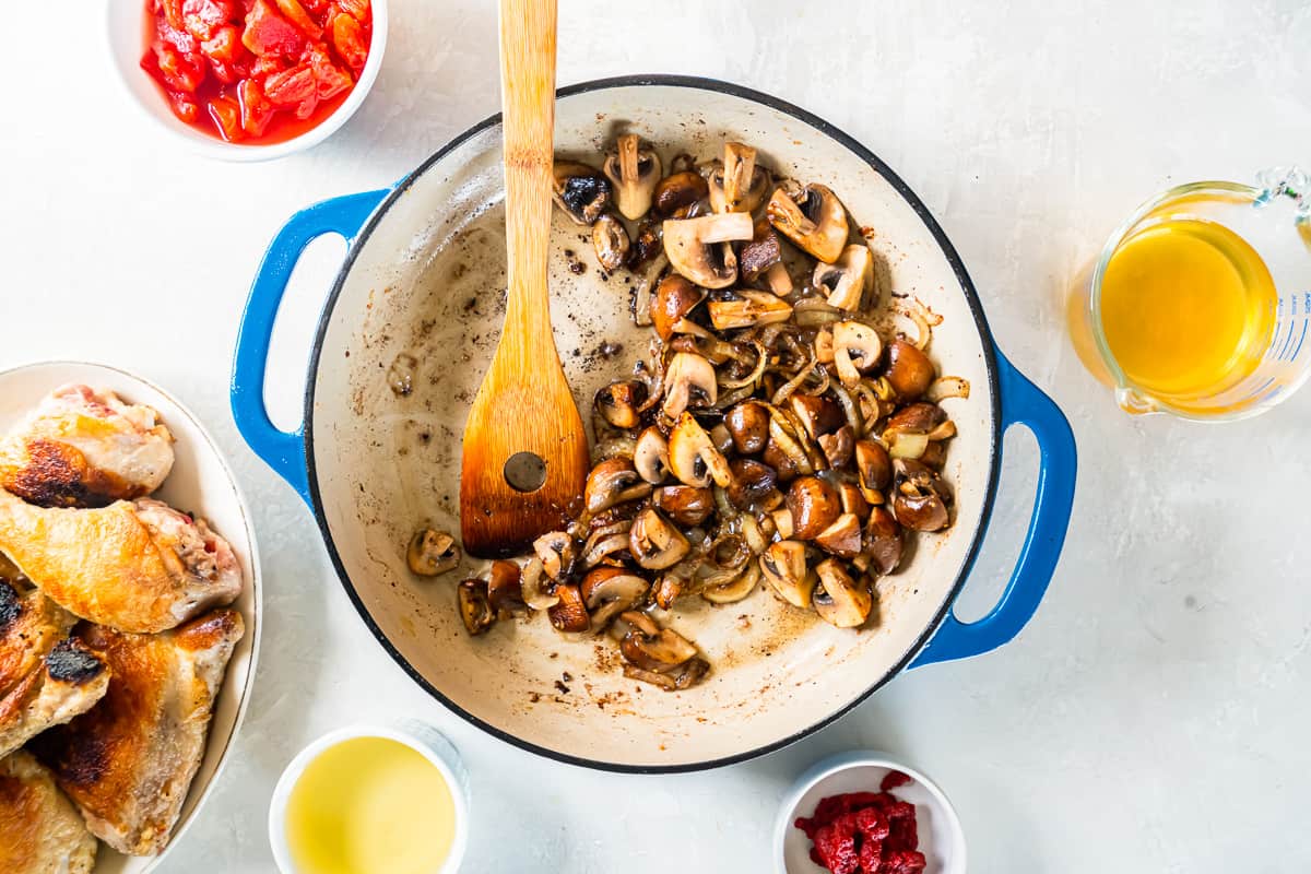 cooked onions and mushrooms in a blue pan with a wooden spoon.