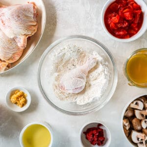 chicken leg quarters dredged in flour in a glass bowl.