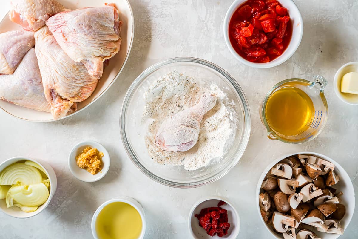 chicken leg quarters dredged in flour in a glass bowl.