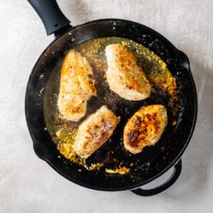 chicken thighs cooking in a cast iron skillet.