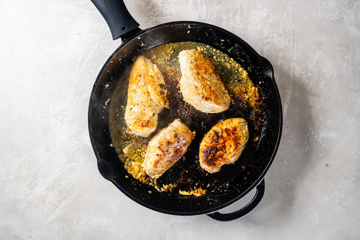 chicken thighs cooking in a cast iron skillet.