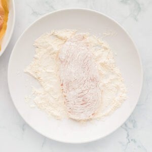 chicken dredged in flour on a white plate.