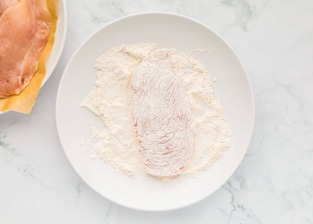 chicken dredged in flour on a white plate.