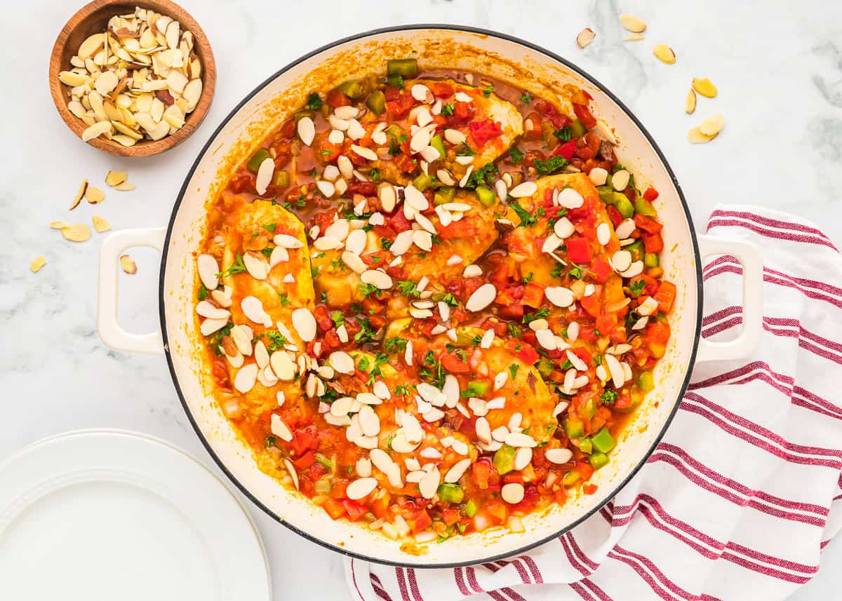 slivered almonds sprinkled over country captain chicken in a pan.