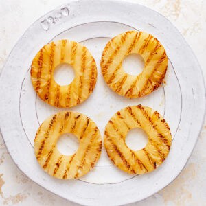 overhead view of grilled pineapple rings on a white plate.