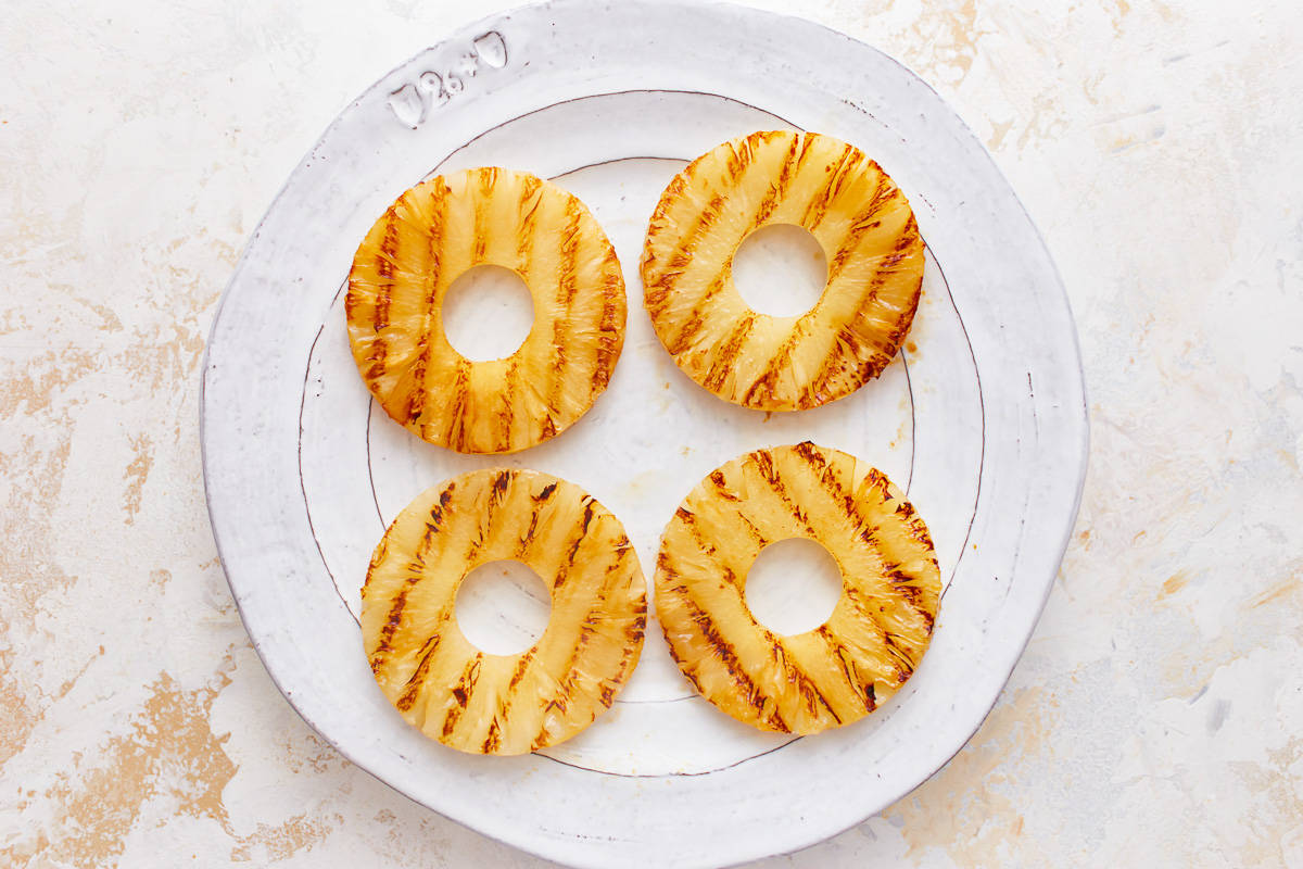 overhead view of grilled pineapple rings on a white plate.