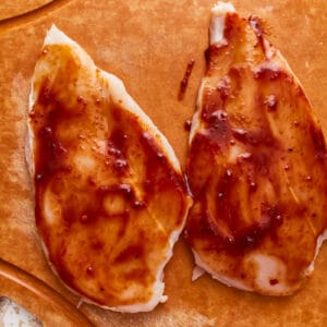 2 raw chicken breasts coated in BBQ sauce.