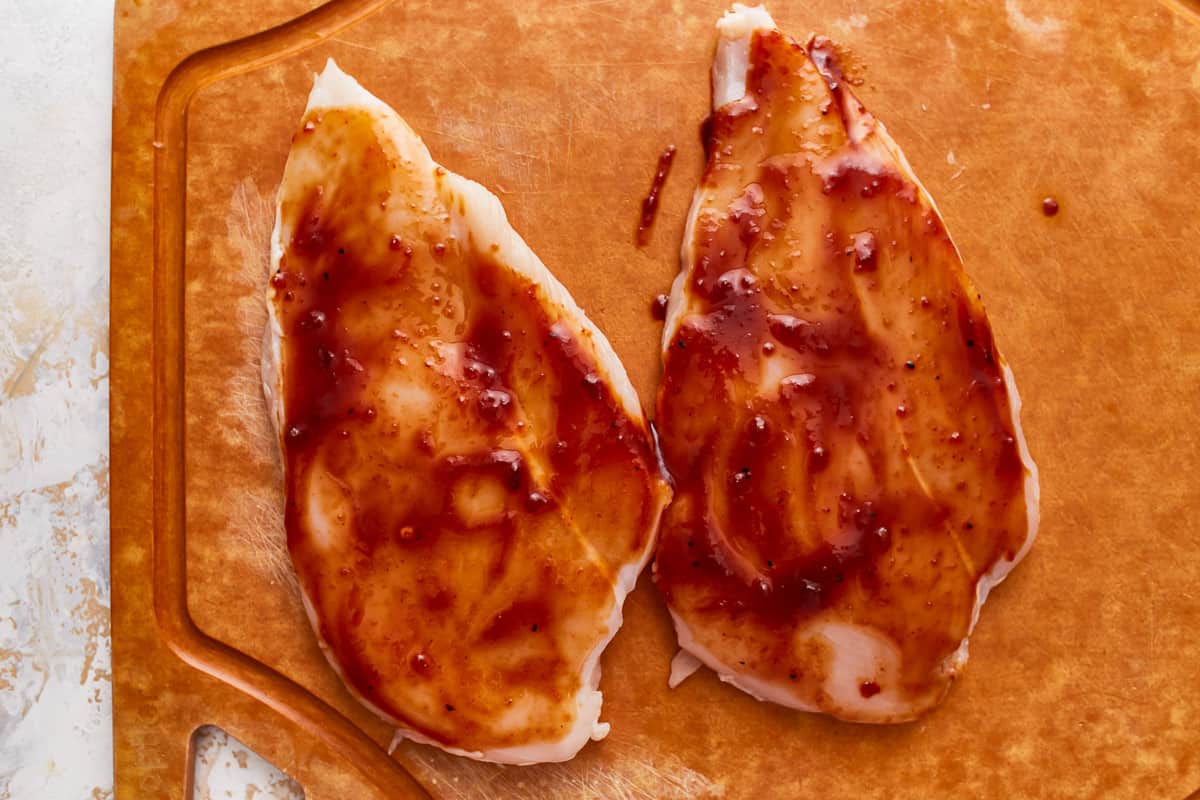 2 raw chicken breasts coated in BBQ sauce.