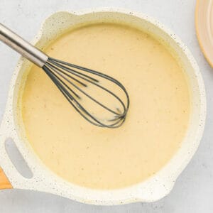 creamy yellow sauce in a white pan with a whisk.