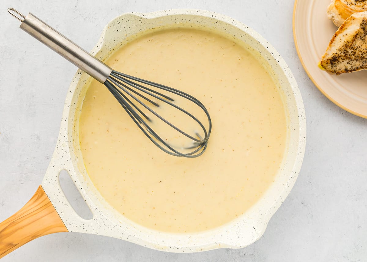 creamy yellow sauce in a white pan with a whisk.