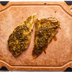 raw pesto-coated chicken breasts on a cutting board.