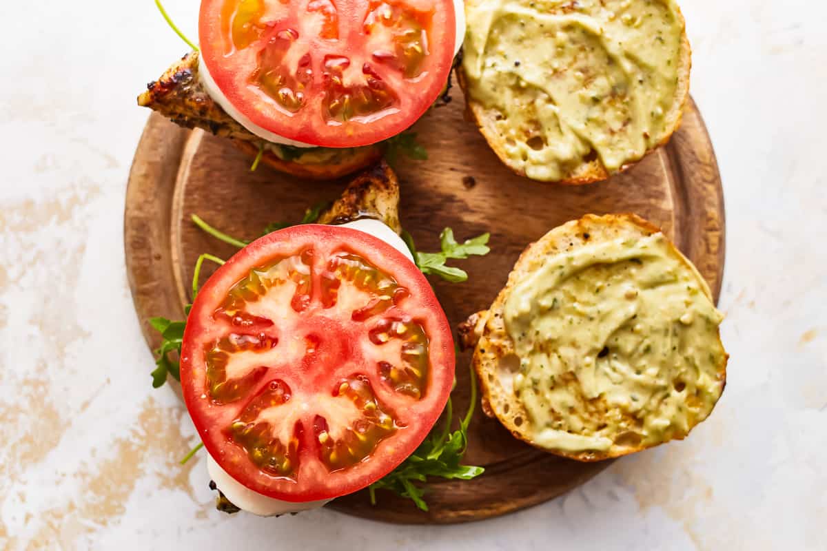 open pesto chicken sandwiches on a cutting board.