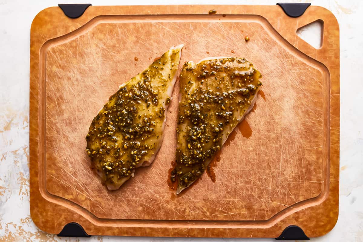 raw pesto-coated chicken breasts on a cutting board.