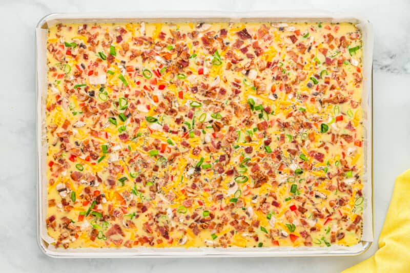 meat and veggies sprinkled over seasoned eggs in a sheet pan.