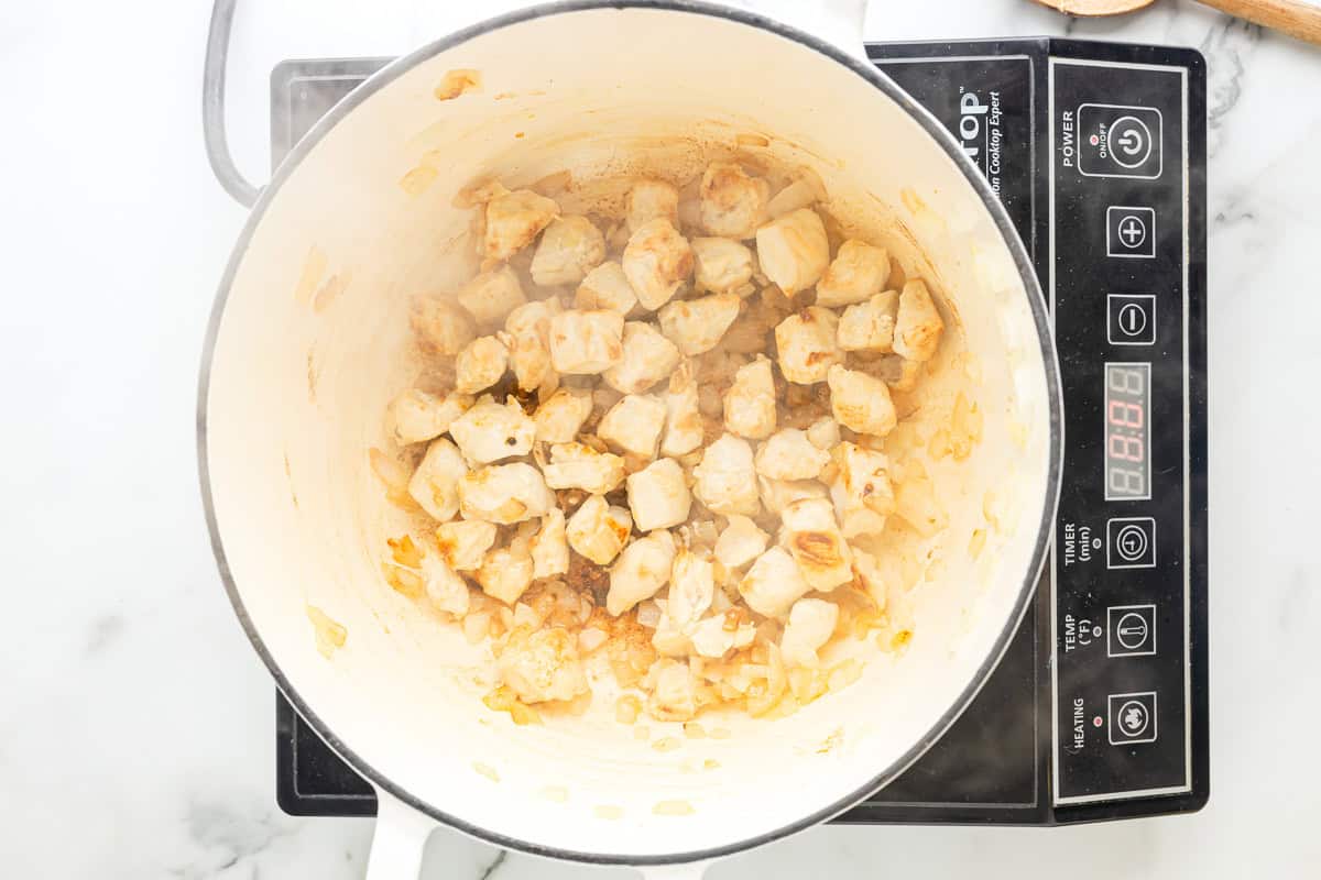 cooked chunks of chicken and onion in a dutch oven.