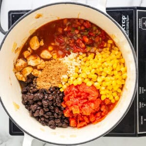 salsa, corn, tomatoes, beans, and seasonings added to cooked chicken chunks in a dutch oven.