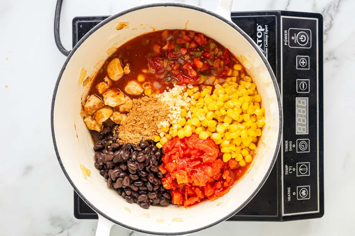 salsa, corn, tomatoes, beans, and seasonings added to cooked chicken chunks in a dutch oven.