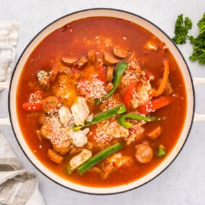 sauce poured over chicken, sausage, and veggies in a pan.