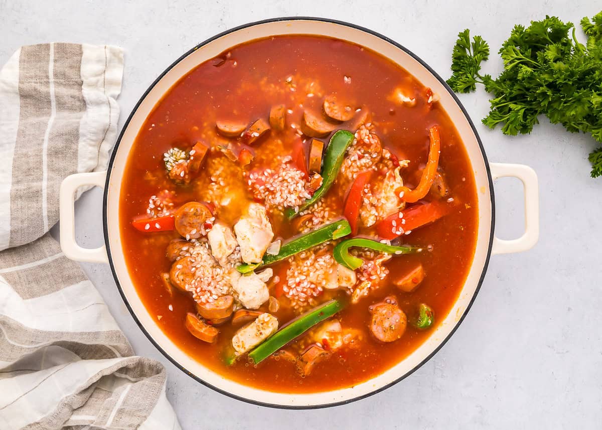 sauce poured over chicken, sausage, and veggies in a pan.