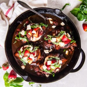 strawberry balsamic chicken topped with cheese and basil in a pan with a spoon.