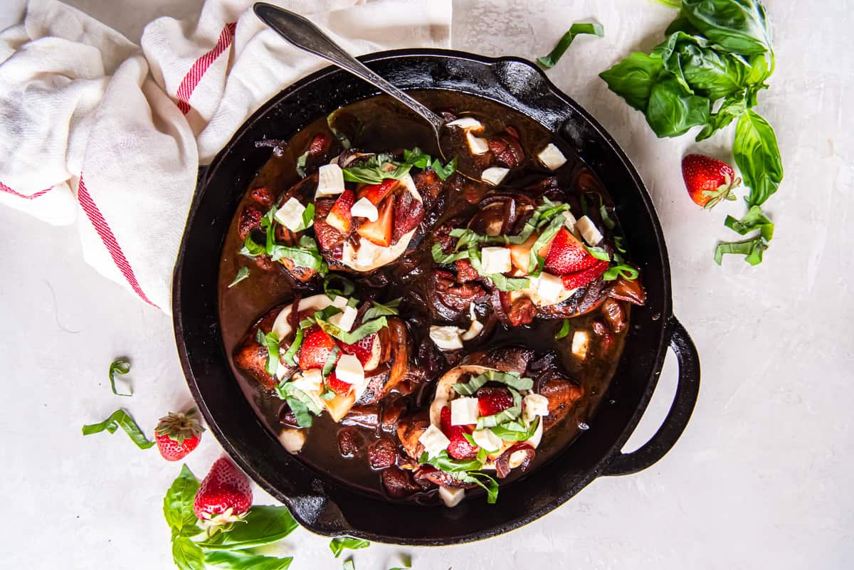 strawberry balsamic chicken topped with cheese and basil in a pan with a spoon.