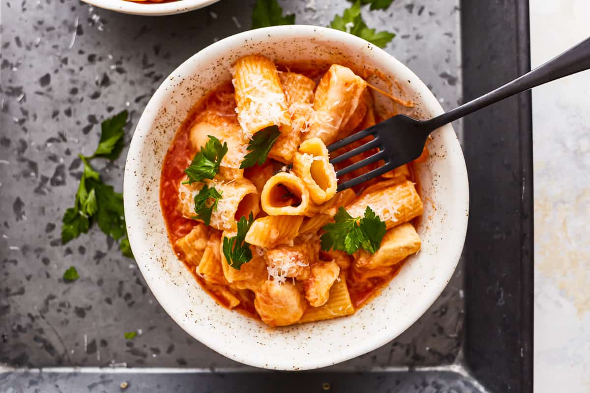 overhead view of a fork stabbing instant pot chicken parmesan pasta in a white bowl.