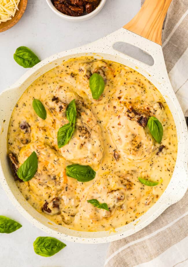 overhead view of marry me chicken topped with fresh basil leaves in a white pan.