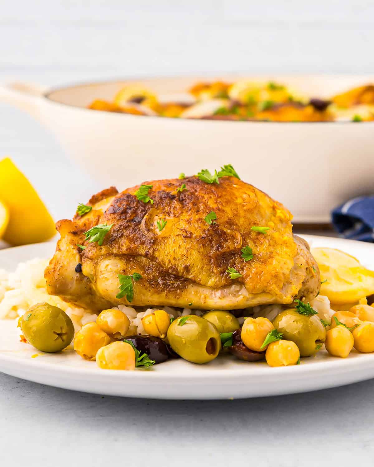 side view of a serving of moroccan chicken thighs on a white plate.