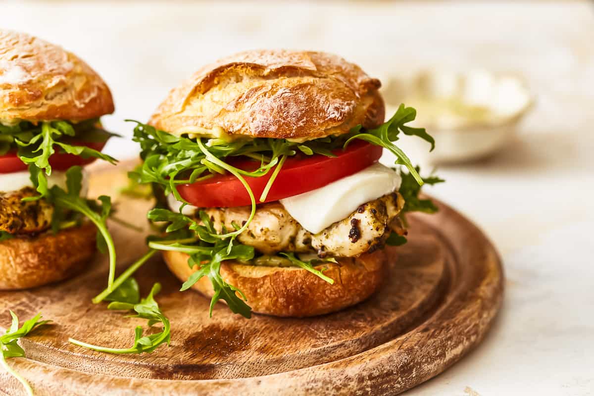 a pesto chicken sandwich on a wooden cutting board.