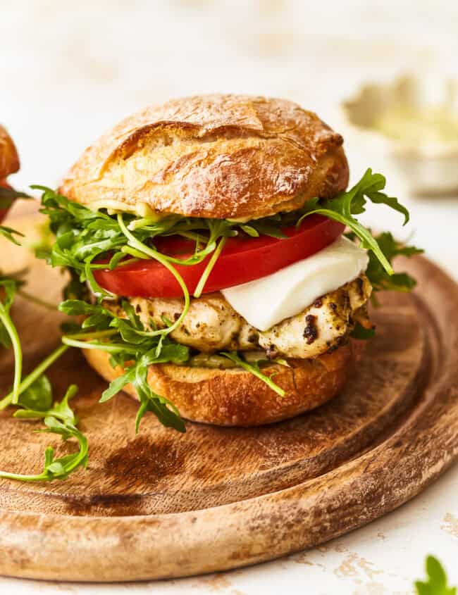 a pesto chicken sandwich on a wooden cutting board.