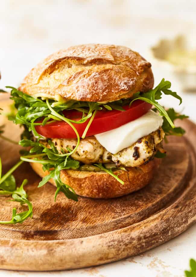 a pesto chicken sandwich on a wooden cutting board.