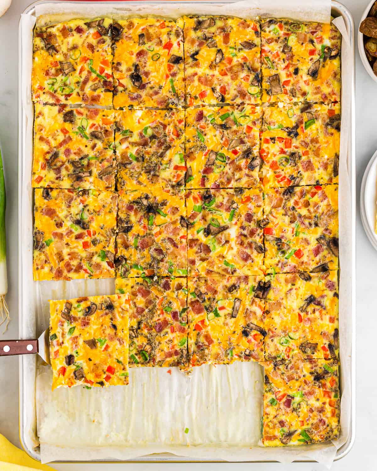 a spatula lifting a serving of sheet pan eggs from a pan.