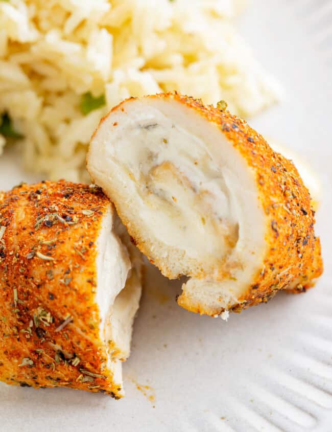 a halved chicken roll up on a white plate with rice.