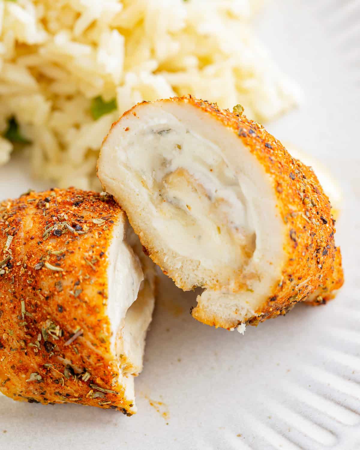 a halved chicken roll up on a white plate with rice.