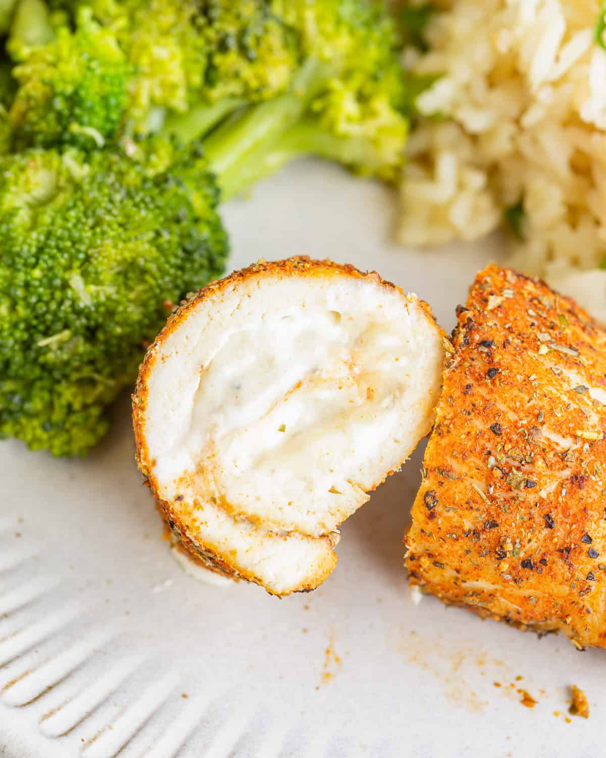 a halved chicken roll up on a white plate with rice and broccoli.