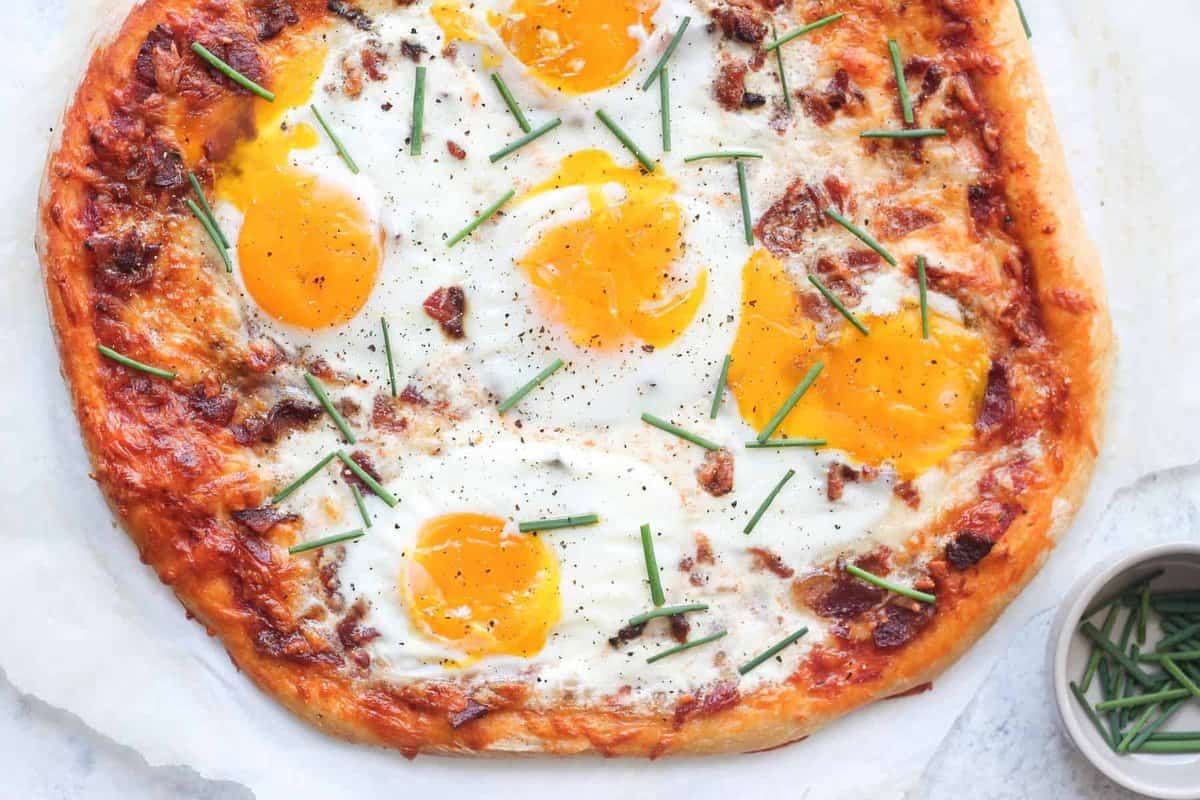 A breakfast pizza with eggs and sprigs of rosemary.