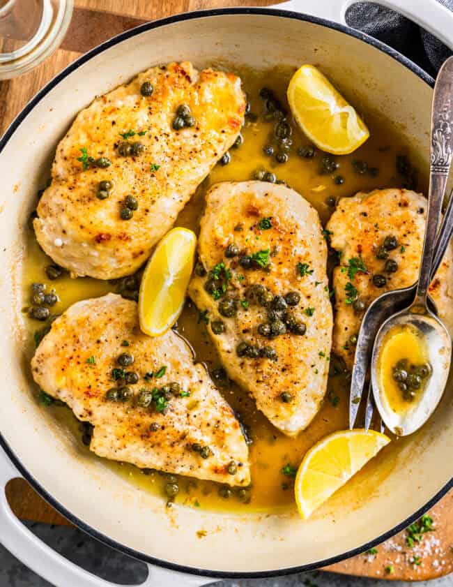 chicken piccata with lemon and spoon in white skillet