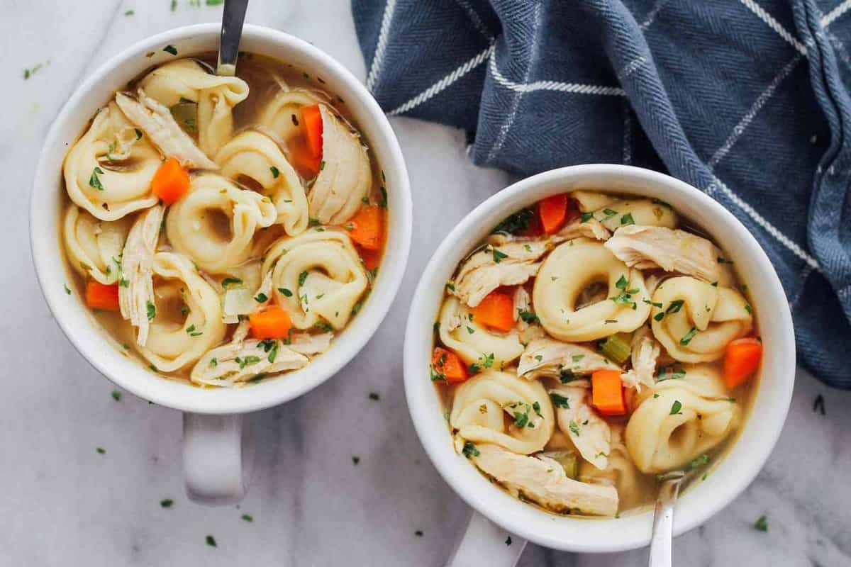 Two bowls of chicken tortellini soup with carrots and noodles.