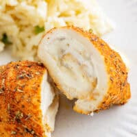 a halved chicken roll up on a white plate with rice.