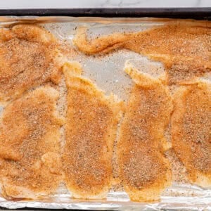 seasoned thin sliced chicken breasts on a baking sheet.