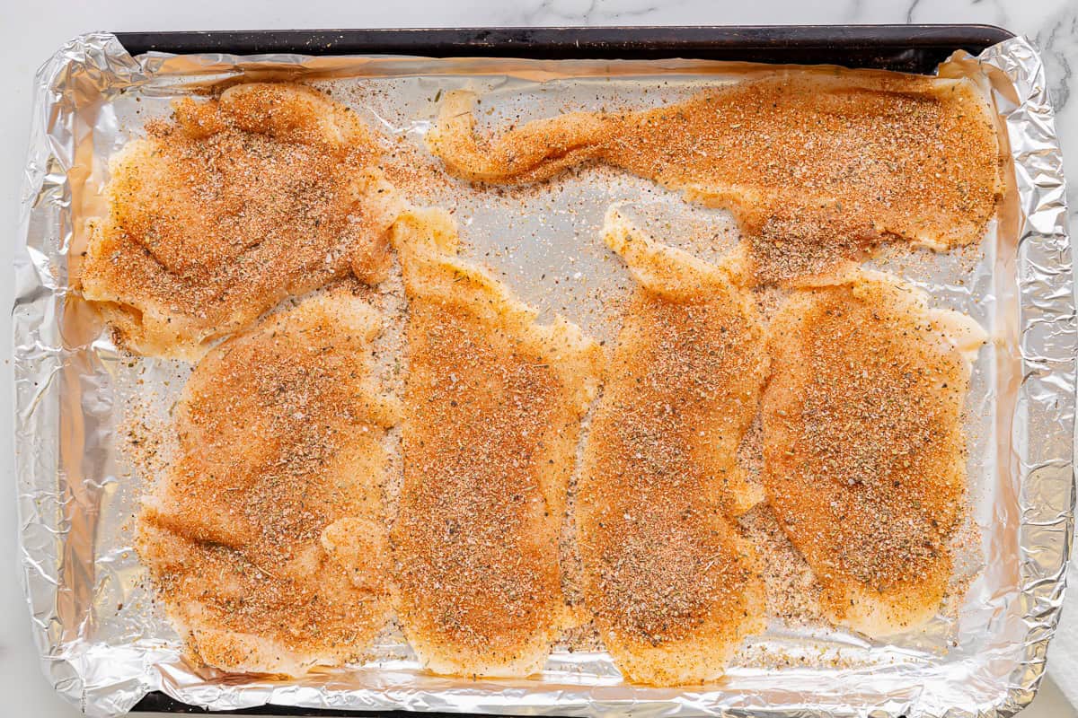 seasoned thin sliced chicken breasts on a baking sheet.