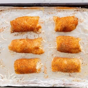 seasoned chicken breasts rolled up with boursin and mozzarella on a baking sheet.