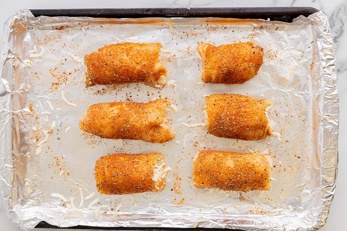 seasoned chicken breasts rolled up with boursin and mozzarella on a baking sheet.