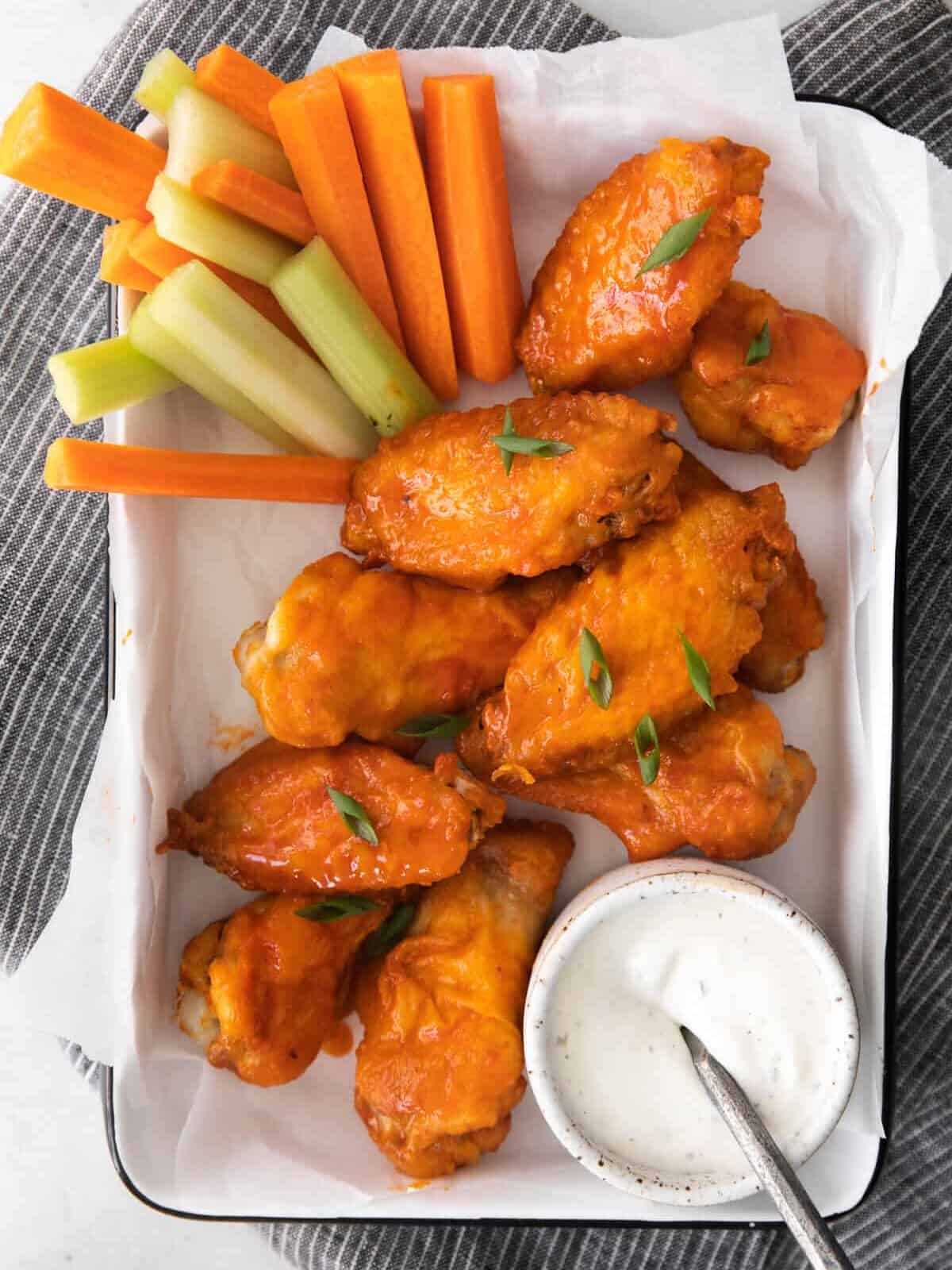 overhead image of honey buffalo chicken wings on a serving tray with sliced carrots and celery and dressing in a small bowl