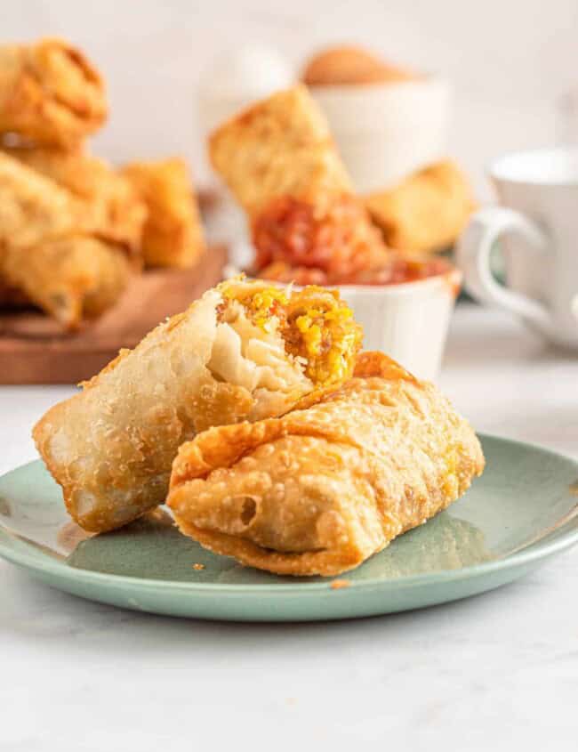 two breakfast egg rolls on a plate, one with a bite taken out