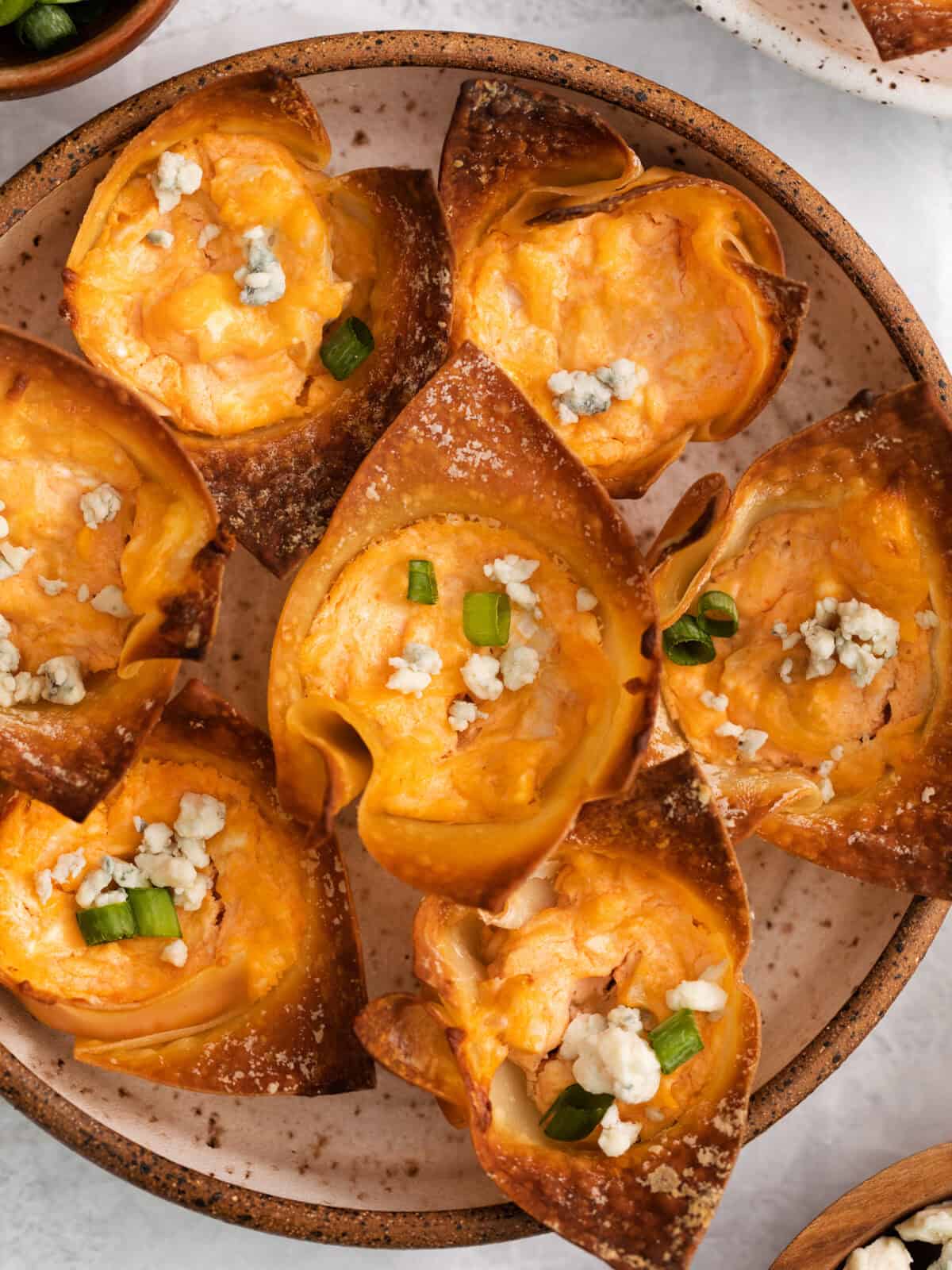 overhead view of buffalo chicken wonton cups on a white and brown plate.