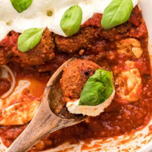 wood spoon held over a baking dish filled with chicken parmesan meatballs with one meatball on the spoon