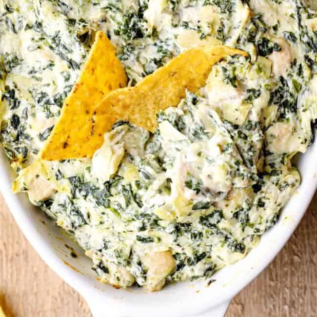 overhead image of chicken spinach artichoke dip in a white baking dish with tortilla chips